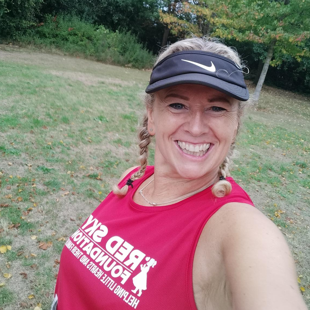 A picture of Emma looking really happy in a red running vest. She has blonde plaits and black peaked cap.
