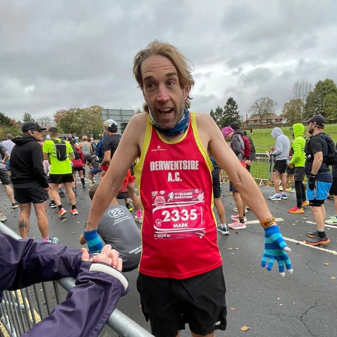 A picture of Mark at the start of a race. He is next to crown barrier and is pulling a funny face, shrugging his shoulders.