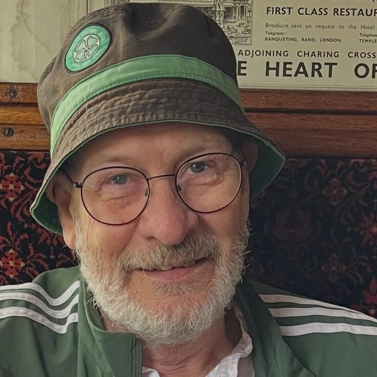A headshot of Mick McGlone. He is wearing a celtic hat and jacket and he is wearing glasses.